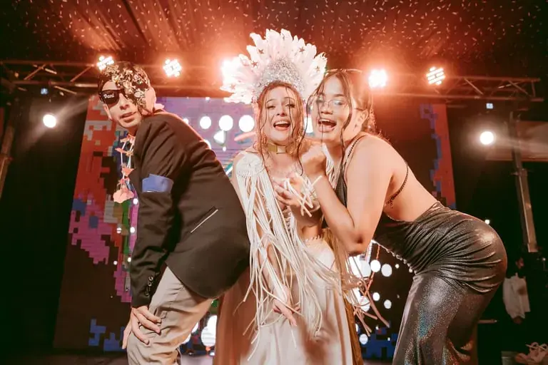 Bailarina con tocado de plumas riendo con dos invitados en la tarima